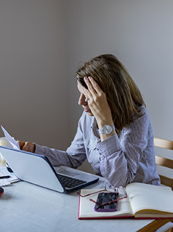 Femme inquiète consultant des papiers devant son ordinateur portable - MACSF