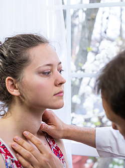 Une médecin examine le cou d’une femme en palpant sa gorge dans un cabinet médical - MACSF