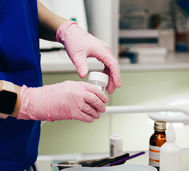 Gros plan sur les mains gantées d'une technicienne de laboratoire tenant un flacon de prélèvement - MACSF