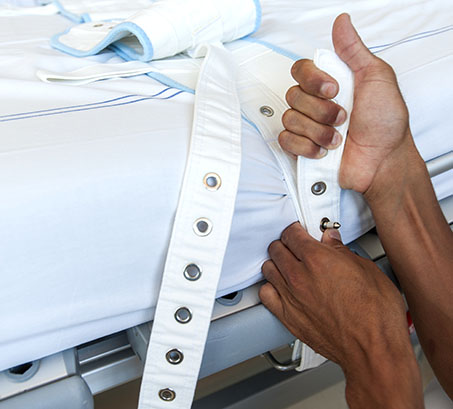 Un professionnel de santé installe des liens de contention sur un lit - MACSF