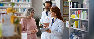 Deux pharmaciens souriants conseillent une cliente âgée - MACSF