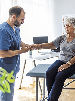 Le médecin examine le poignet d'une patiente âgée assise sur la table d'examen - MACSF