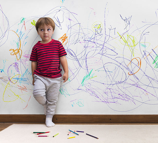 Un enfant, adossé au mur sur lequel il vient de dessiner, regarde son parent d'un air désolé - MACSF