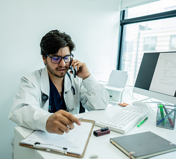 Médecin assis à son bureau et parlant au téléphone - MACSF
