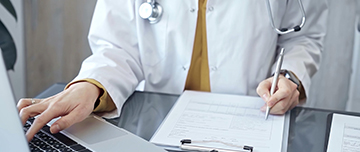 Médecin en blouse blanche saisi des informations sur son ordinateur - MACSF