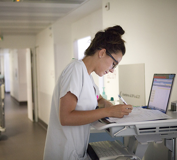 Un infirmière remplissant un dossier posé sur le chariot dans le couloir de l'hôpital - MACSF