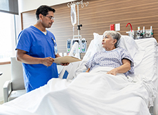Une patiente dans son lit d'hopital discute avec un soignant tenant un dossier médical - MACSF